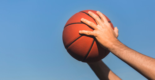 imagen de unas manos de un hombre sosteniendo un balón de baloncesto en posición de lanzamiento a canasta
