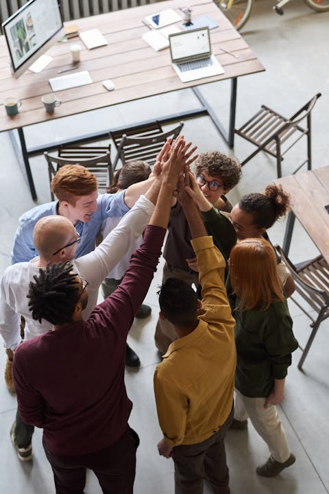 imagen de un grupo de personas trabajando uniendo los brazos en símbolo de unión y celebración como equipo de trabajo